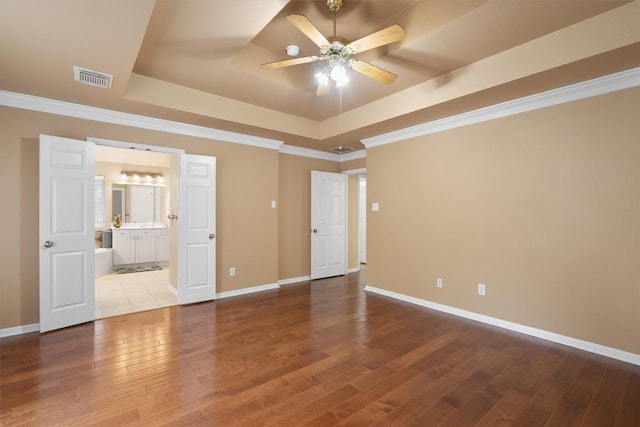 empty room with ceiling fan, a raised ceiling, wood-type flooring, and ornamental molding