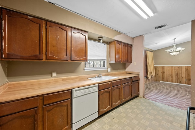 kitchen with wooden walls, sink, decorative light fixtures, dishwasher, and a chandelier