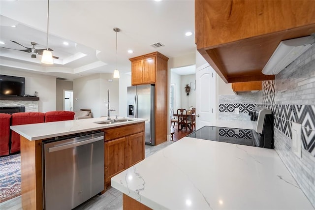 kitchen with ceiling fan, stainless steel appliances, an island with sink, pendant lighting, and a fireplace