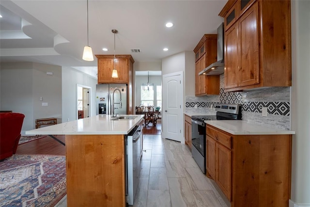 kitchen featuring wall chimney exhaust hood, a breakfast bar, stainless steel appliances, hanging light fixtures, and an island with sink