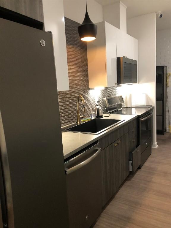 4361 S Congress Ave Unit 106, Austin, TX 78745 - kitchen with stainless steel appliances, wood finished floors, decorative backsplash, hanging light fixtures, and light countertops