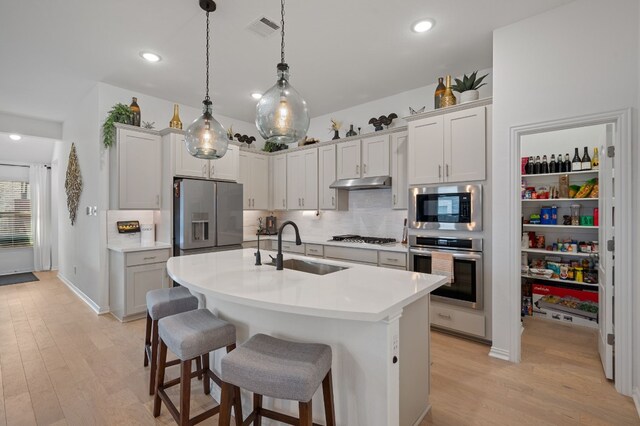 kitchen featuring a kitchen bar, tasteful backsplash, hanging light fixtures, an island with sink, and stainless steel appliances