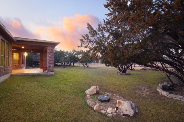 yard at dusk featuring ceiling fan