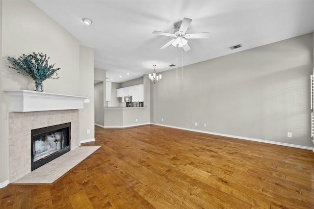 unfurnished living room featuring ceiling fan with notable chandelier, light hardwood / wood-style floors, and a tile fireplace