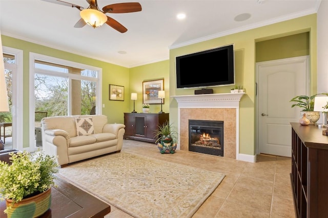 living room featuring light tile patterned floors, ceiling fan, crown molding, and a tiled fireplace