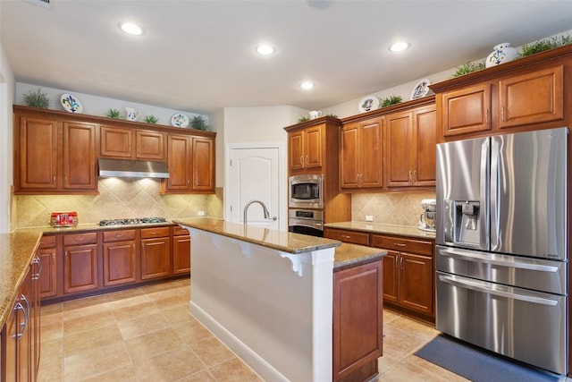 kitchen featuring decorative backsplash, light stone counters, an island with sink, and appliances with stainless steel finishes