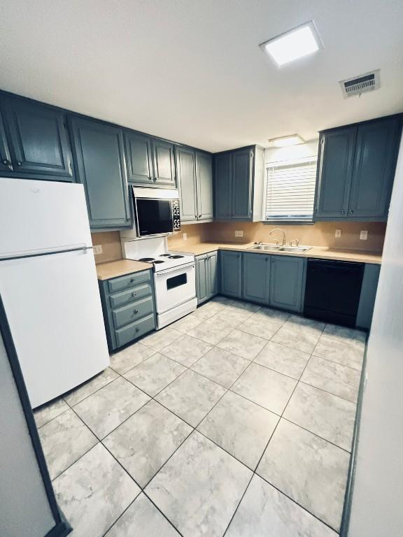 kitchen with blue cabinetry, sink, light tile patterned flooring, and white appliances