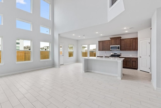 kitchen featuring a kitchen island with sink, a high ceiling, sink, decorative backsplash, and stainless steel appliances