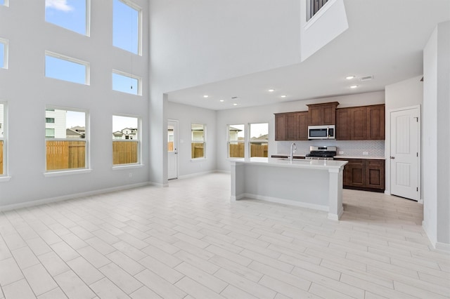 kitchen featuring appliances with stainless steel finishes, a towering ceiling, an island with sink, sink, and decorative backsplash