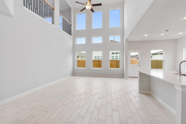 unfurnished living room with a towering ceiling, ceiling fan, and sink