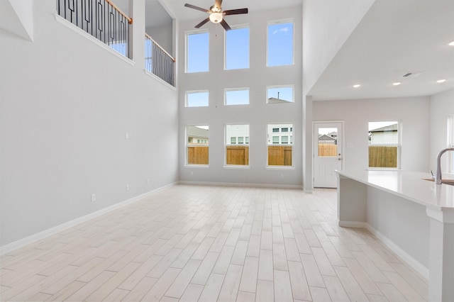 unfurnished living room featuring a towering ceiling, sink, and ceiling fan