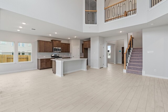 kitchen with light wood-type flooring, a towering ceiling, stainless steel appliances, and an island with sink