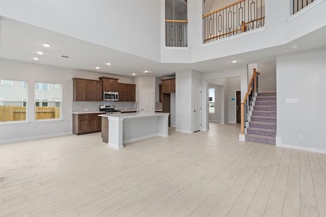 kitchen with a towering ceiling, stainless steel appliances, light hardwood / wood-style floors, and a center island with sink