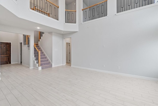 unfurnished living room featuring a towering ceiling and light hardwood / wood-style flooring