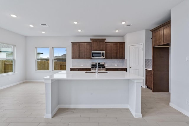 kitchen with decorative backsplash, sink, stainless steel appliances, and an island with sink