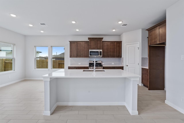 kitchen featuring sink, appliances with stainless steel finishes, dark brown cabinets, tasteful backsplash, and a center island with sink