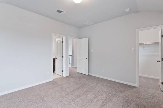 unfurnished bedroom with a walk in closet, a closet, light colored carpet, and lofted ceiling