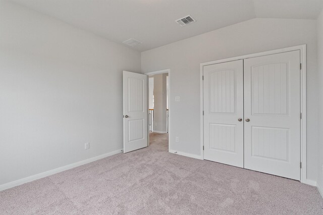 unfurnished bedroom featuring light colored carpet, vaulted ceiling, and a closet