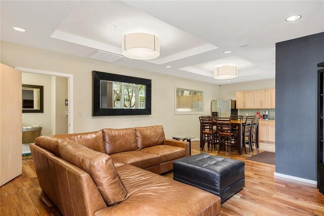 living room featuring light wood-type flooring and a tray ceiling