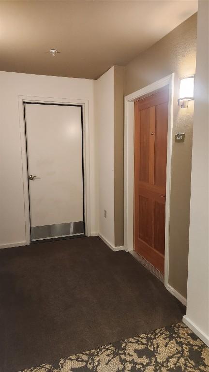 doorway to outside with baseboards and dark carpet