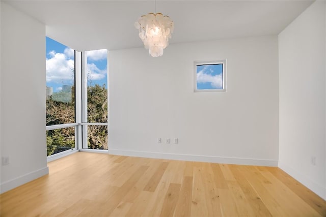 unfurnished room featuring a notable chandelier, expansive windows, baseboards, and wood finished floors