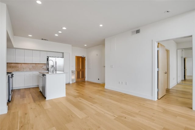 kitchen featuring light wood finished floors, stainless steel appliances, visible vents, backsplash, and an island with sink