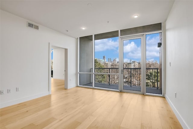 unfurnished room featuring a city view, wood finished floors, visible vents, baseboards, and floor to ceiling windows