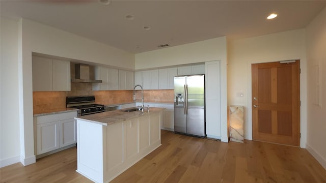 kitchen with wall chimney exhaust hood, appliances with stainless steel finishes, a sink, and decorative backsplash