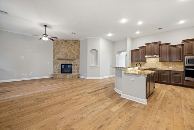 kitchen featuring light stone counters, tasteful backsplash, a center island with sink, light wood-type flooring, and appliances with stainless steel finishes