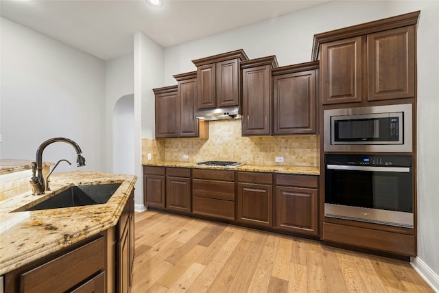 kitchen with sink, decorative backsplash, light stone counters, stainless steel appliances, and light wood-type flooring