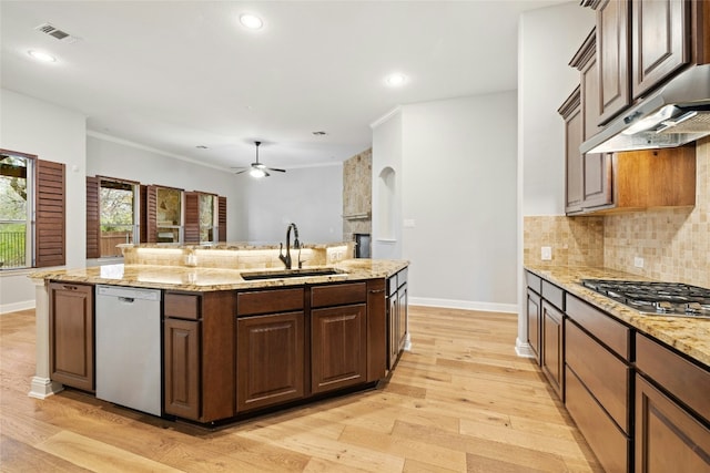 kitchen with sink, appliances with stainless steel finishes, light stone countertops, a kitchen island with sink, and decorative backsplash