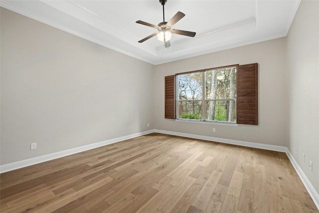 empty room with ceiling fan, light wood-type flooring, and a tray ceiling