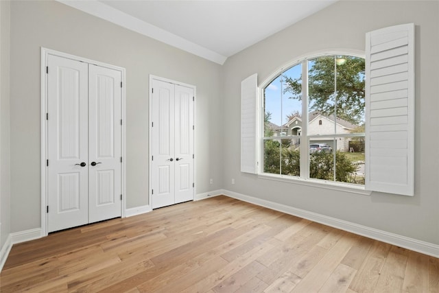 unfurnished bedroom featuring light hardwood / wood-style floors and two closets