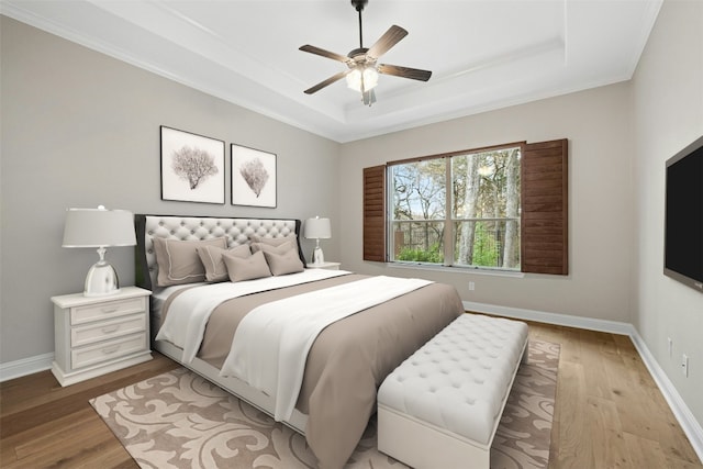 bedroom with ceiling fan, a tray ceiling, and light wood-type flooring