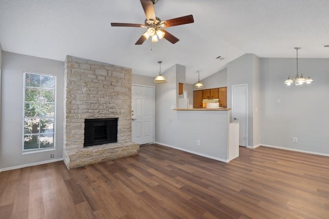 unfurnished living room with a stone fireplace, ceiling fan with notable chandelier, lofted ceiling, and hardwood / wood-style flooring