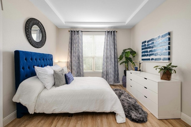 bedroom with light hardwood / wood-style floors and a tray ceiling