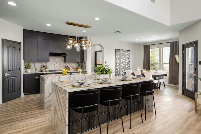 kitchen featuring a large island, sink, tasteful backsplash, pendant lighting, and a breakfast bar area