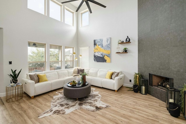 living room featuring ceiling fan, light wood-type flooring, a towering ceiling, and a fireplace