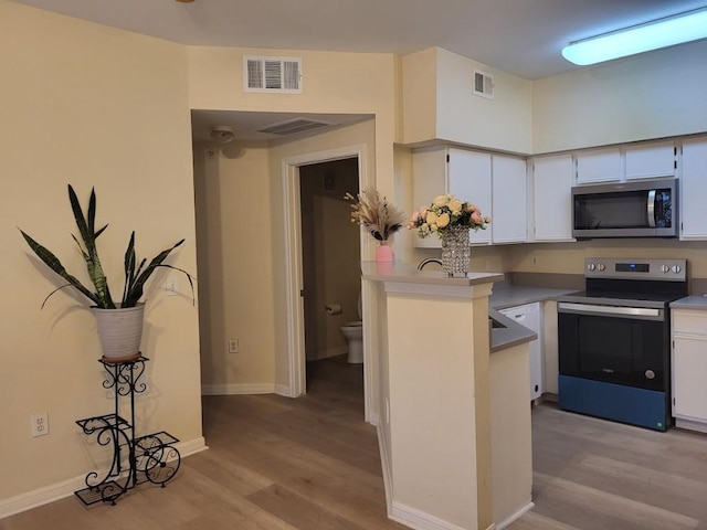 kitchen with kitchen peninsula, stainless steel appliances, white cabinetry, and light hardwood / wood-style flooring