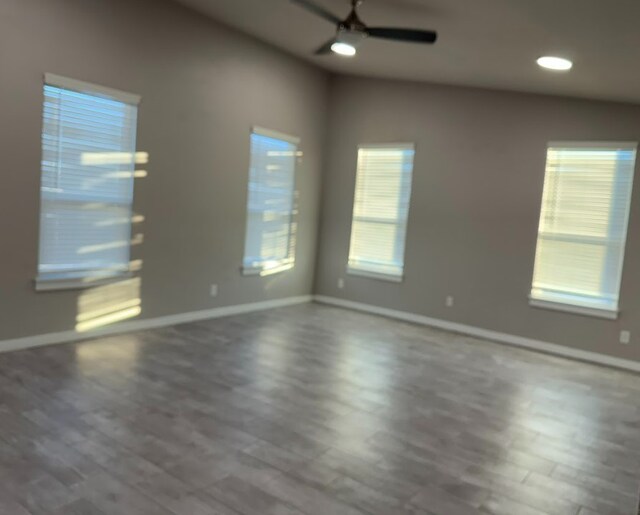 unfurnished room featuring a healthy amount of sunlight, ceiling fan, and dark wood-type flooring