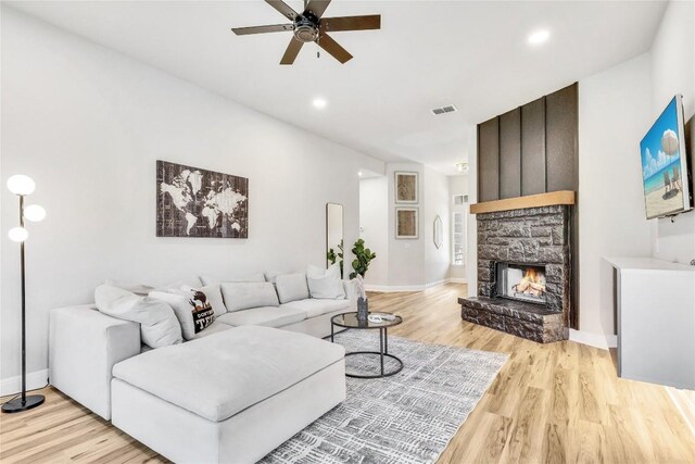 living room featuring light hardwood / wood-style floors, a stone fireplace, and ceiling fan