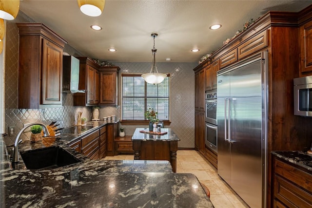 kitchen with sink, wall chimney exhaust hood, dark stone counters, pendant lighting, and appliances with stainless steel finishes