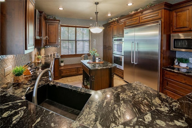 kitchen with sink, a center island, hanging light fixtures, dark stone countertops, and appliances with stainless steel finishes