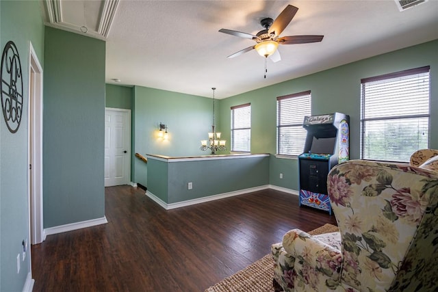 living area featuring ceiling fan with notable chandelier and dark wood-type flooring