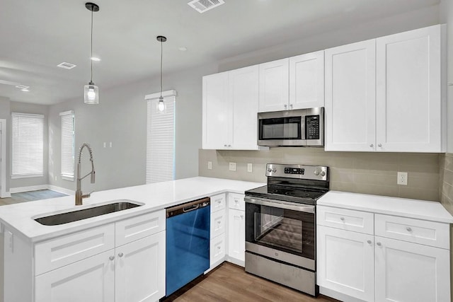 kitchen featuring white cabinets, sink, appliances with stainless steel finishes, decorative light fixtures, and kitchen peninsula