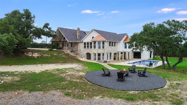 rear view of property featuring a lawn, a patio area, and an outdoor fire pit