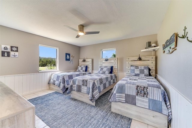 bedroom with ceiling fan, light tile patterned floors, and a textured ceiling