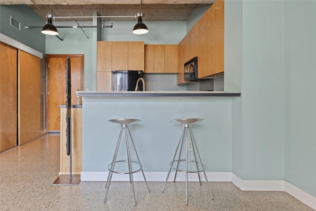 kitchen featuring a kitchen bar, kitchen peninsula, stainless steel fridge, and hanging light fixtures