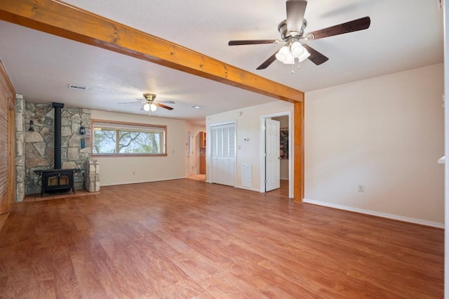 unfurnished living room featuring ceiling fan, a wood stove, and light hardwood / wood-style flooring