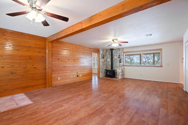 unfurnished living room with a textured ceiling, wood-type flooring, beamed ceiling, a wood stove, and wood walls